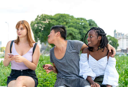 A young woman being left out sitting in a park with friends checking her phone.の写真素材