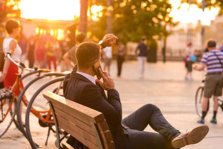 A businessmen sitting on a bench and talking on his phoneの写真素材