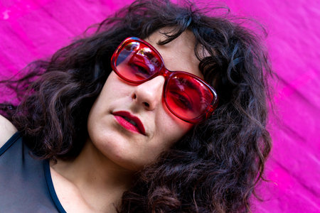 Young woman portrait wearing red sunglasses at a pink brick wallの写真素材