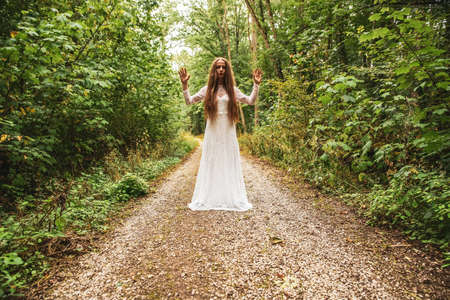 A woman standing in the forest and reaching up