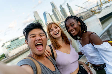 Young friends taking selfies at the riverside skyscrapers in the background.の写真素材
