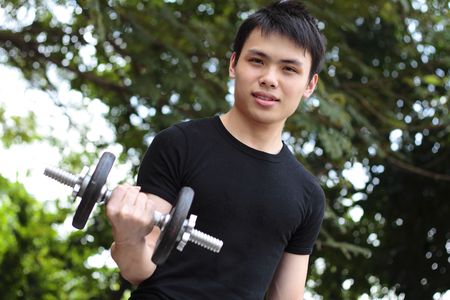 A young Asian man exercising with a dumb bell outdoorsの写真素材