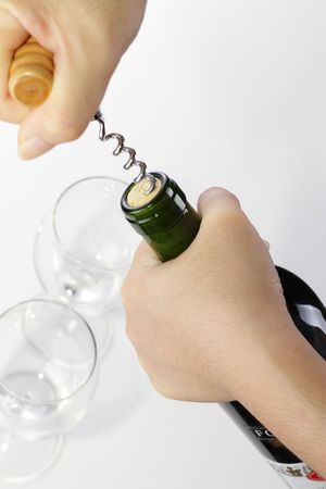 A woman opening a bottle of wine with a corkscrew. Two empty wine glasses are in the backgroundの写真素材