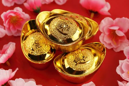 Top view of some chinese gold ingots surrounded by cherry blossoms on a red backgroundの写真素材