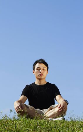 A young Asian man meditating outdoors on a sunny dayの写真素材