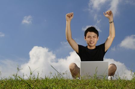 A college student and a laptop with his arms raised in triumphの写真素材