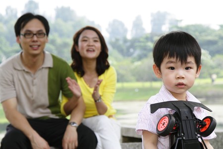 An Asian boy playing with his toy as his parents watch onの写真素材