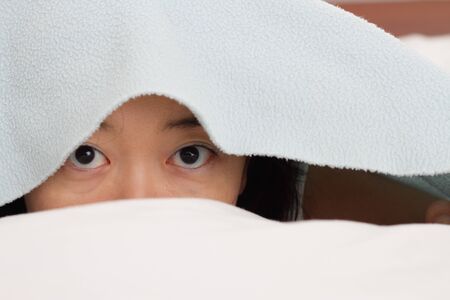 An Asian woman in bed under a blanketの写真素材