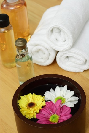 A wooden bowl with flowers and some spa items in the backgroundの写真素材
