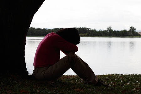 A depressed Asian woman sitting by a treeの写真素材