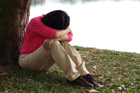 A depressed Asian woman sitting by a treeの写真素材