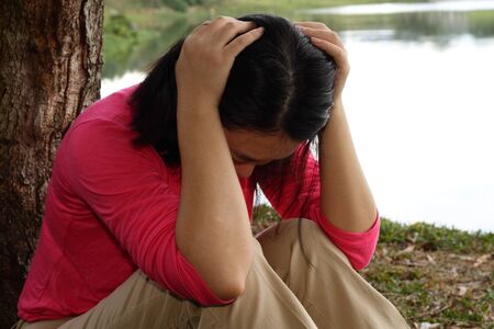 A depressed Asian woman sitting by a treeの写真素材