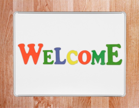 Colorful cut-out wooden letters spelling out 'Welcome' placed on a magnetic whiteboard against wooden background, clipping path around whiteboardの写真素材