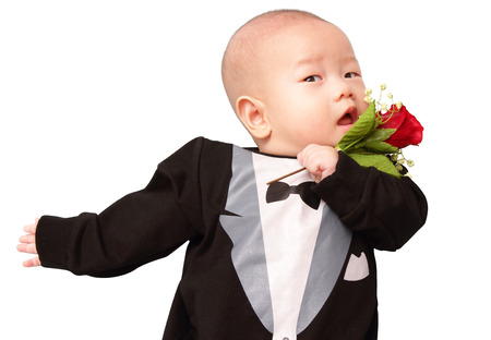 A baby wearing a tuxedo costume holding a roseの写真素材