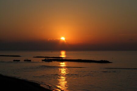 Scenic view of sunset over Cyprus island coastline with boats silhouetted in black.の写真素材