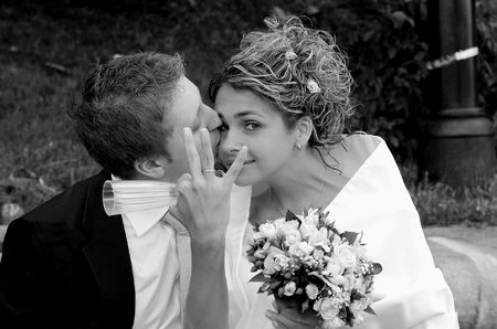 Newlywed groom kissing bride who is holding gls and showing off wedding ring, outdoors.の写真素材