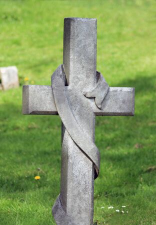 Memorial cross gravestone in cemetery with green grass in background.の写真素材