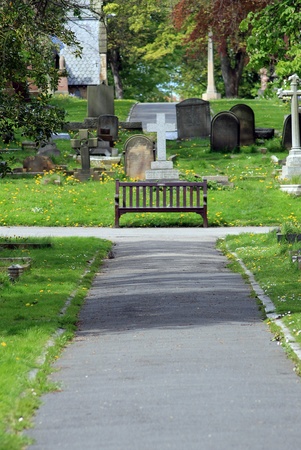 Path and bench in old cemetery with church and gravestones.の写真素材