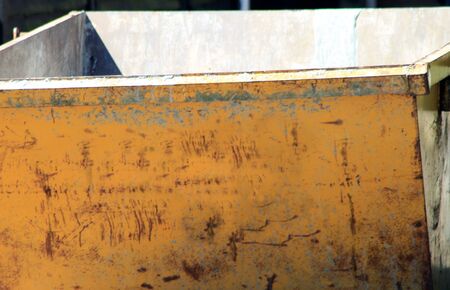 Front of old empty yellow refuse skip outdoors.