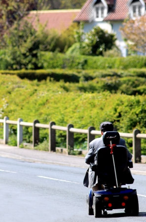Rear view or senior man riding mobility scooter on countryside road.の写真素材