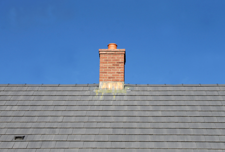 Gray tile roof and chimney on house with blue sky background.の写真素材