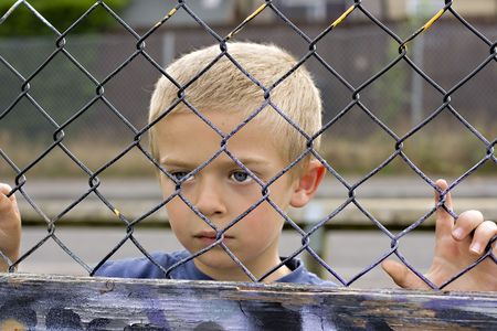 A portrait of a young boy looking through a chain link fenceの写真素材