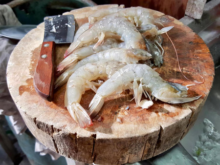 a photography of a wooden cutting board with shrimp on it, there are some shrimp on a wooden board with a knife.の写真素材