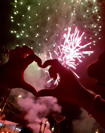 a photography of a person making a heart with their hands, someone making a heart with their hands with fireworks in the background.の写真素材