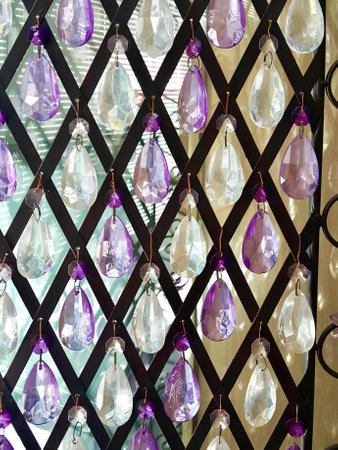 a photography of a wall with a bunch of purple and white glass hanging from it, purple and white glass ornaments hanging on a black lattice.の写真素材
