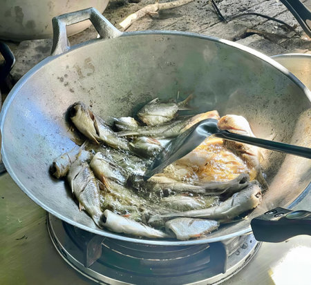 a photography of a pan of fish cooking on a stove, wok with fish cooking in it on a stove top.の写真素材