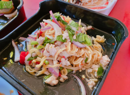 a photography of a plate of noodles with meat and vegetables, carbonarape noodles with vegetables and meat in a black container.の写真素材