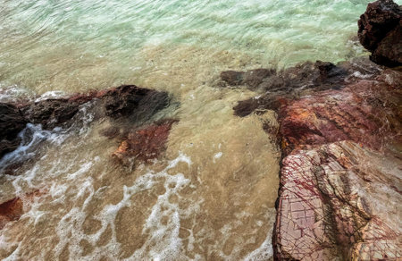 a photography of a beach with a rock formation in the water, sea - coast view of a rocky beach with a wave coming in.の写真素材