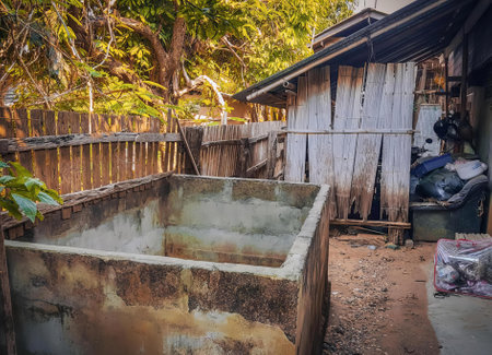 a photography of a dirty bathtub in a backyard with a wooden fence, vat in a dirty yard with a wooden fence and a trash can.の写真素材