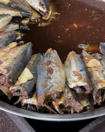 a photography of a pan filled with fish and sauce on a table, hot pot with cooked fish and sauce in...