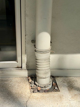 Architectural detail featuring a white corrugated downspout leading to decorative rocks on speckled...