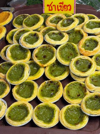 Close-up of numerous vibrant green egg tarts, featuring flaky golden pastry and a rich green custard...