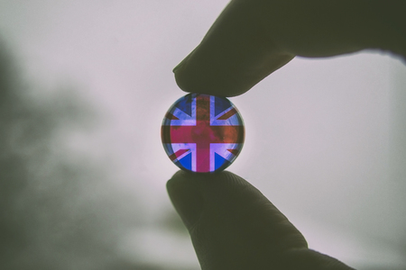 British flag in glass ball in a hand fingers on a light background. English flags in hands.の写真素材