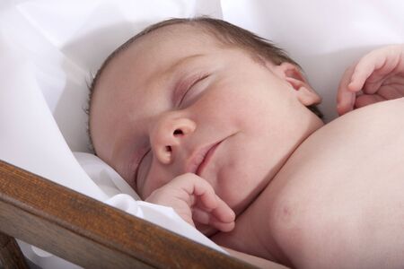 Newborn baby asleep on white blanket in crib.