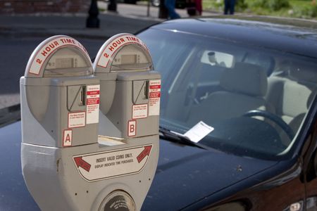 Parking meter with a car in the background with a ticket on the windshieldの写真素材