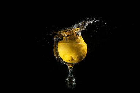 Lemon dropped into glass goblet standing in water making a big splash on a black backgroundの写真素材