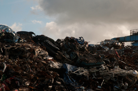 Mountain of scrap metal and metal parts at a landfill with a cloudy sky in the backgroundの写真素材