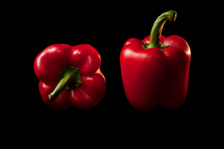 Two red bell peppers in low key lighting, one on its side showing a top view and one standing up showing a side view, on a black backgroundの写真素材