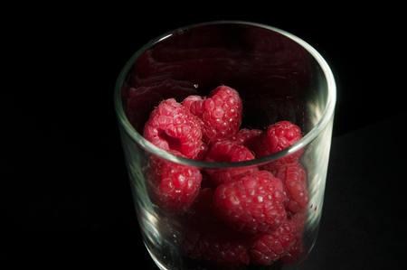 Fancy dessert glass filled with bright fresh red raspberries isolated on a black backgroundの写真素材