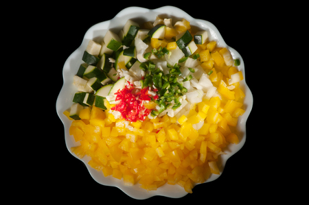 White plate filled with chopped yellow peppers, green jalapeno peppers, red chili peppers, green and white zucchini squash, garlic and onions isolated on a black backgroundの写真素材