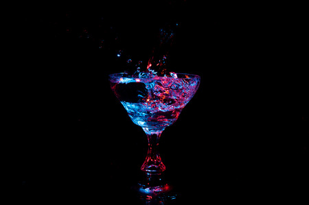 Glowing liquid splashing from champagne glass isolated on a black background