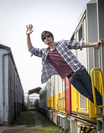 Young man hanging from the train wearing glassesの写真素材