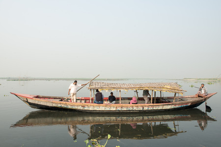 Dhaka, Bangladesh - February 18, 2013: A boat carrying Bengalese dressing in traditional costume moving on black Buriganga River, Dhaka, Bangladesh.のeditorial素材