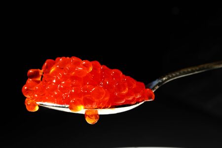 Red caviar in a silver spoon on a black background. Macroの写真素材