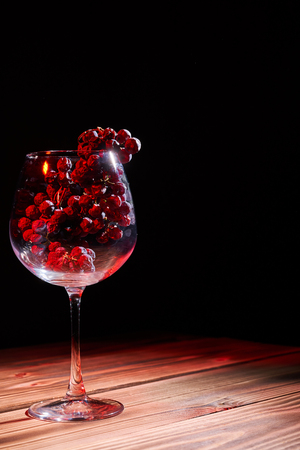 A bunch of ripe grapes in a glass glass glass on a wooden table and a black background.の写真素材