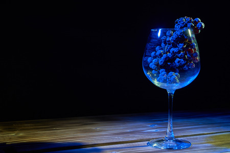 A bunch of ripe grapes in a glass glass glass on a wooden table and a black background.の写真素材
